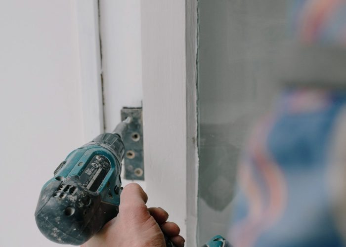 Crop bearded guy installing new wooden window with contemporary screwdriver and metal hinge during renovation process in apartment